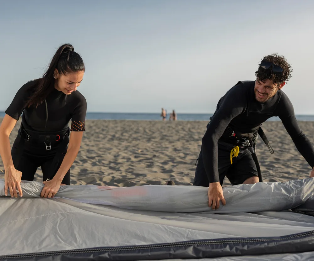 Two kitesurfers rolling up a kite on the beach after a session