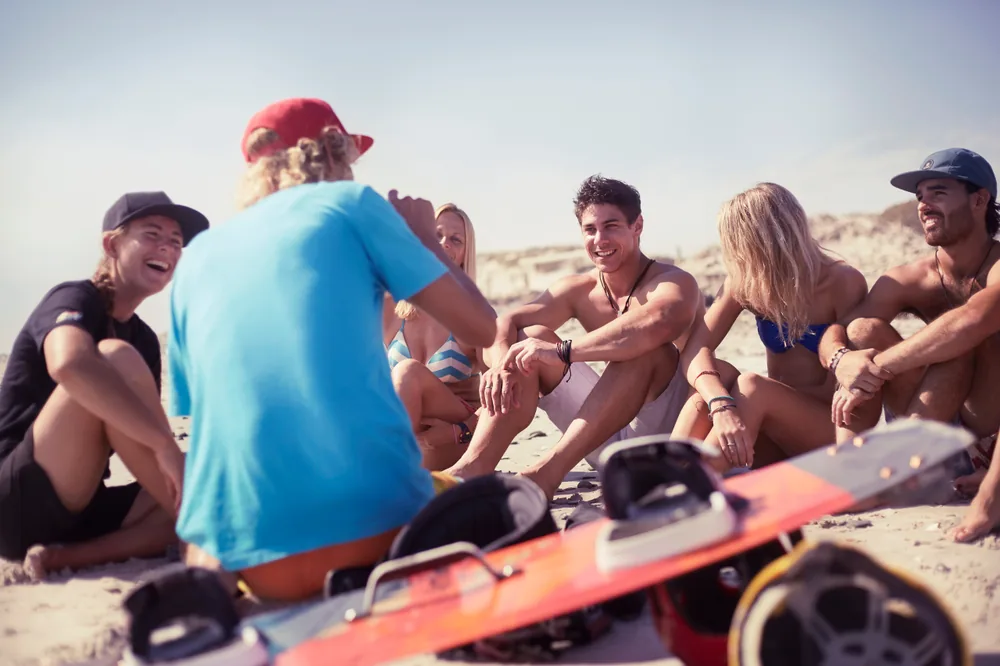 A group chatting on the beach with kiteboarding equipment
